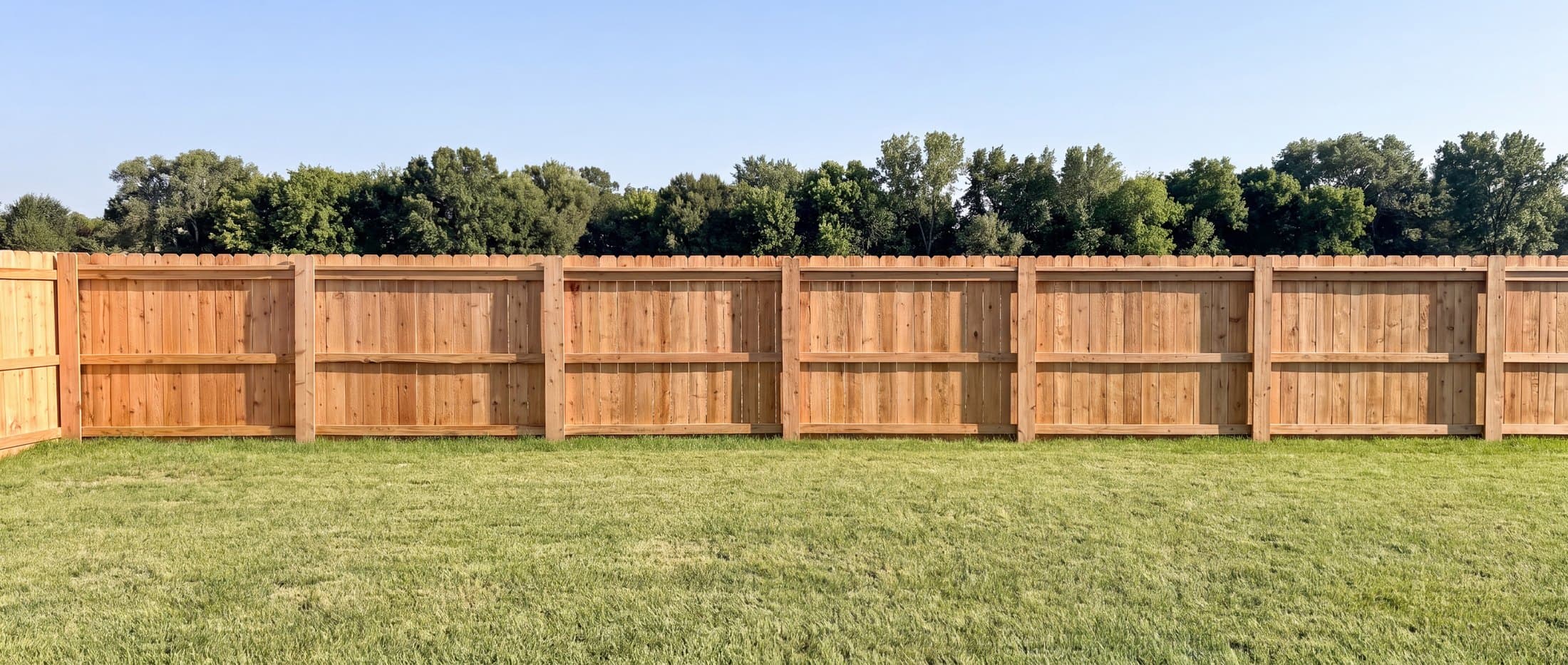 Straight cedar fence run beside a green lawn